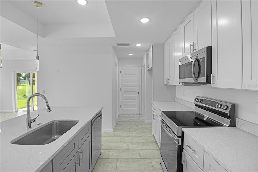 A modern kitchen features white cabinetry, gray lower cabinets, quartz countertops, and stainless steel appliances — 878 NELSON DRIVE, KISSIMMEE, FL