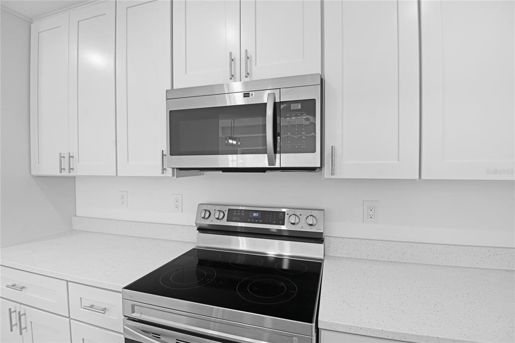 A kitchen features white cabinets, a stainless steel microwave, and a black electric range — 878 NELSON DRIVE, KISSIMMEE, FL