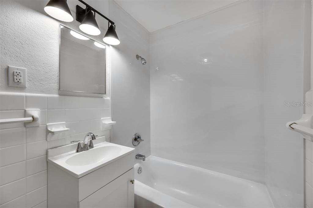 A bathroom features a white vanity, a tiled wall, and a shower-tub combination — 3315 58TH AVENUE S UNIT 103, ST PETERSBURG, FL