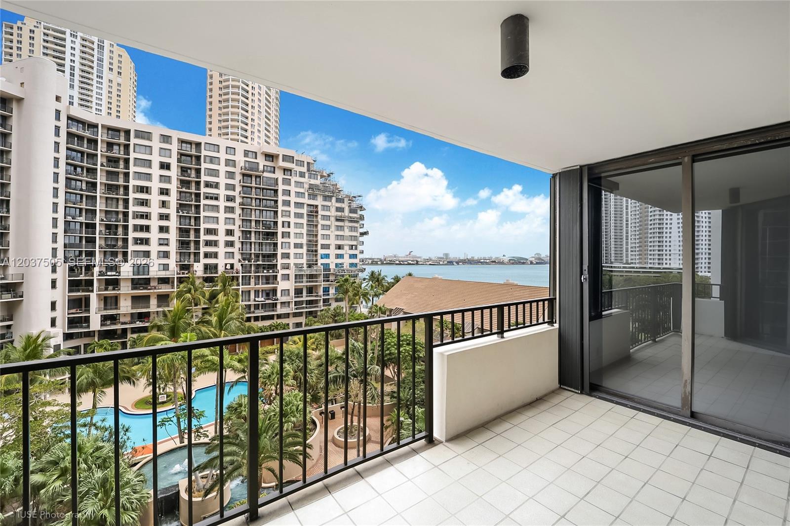A balcony with white tile flooring overlooks a swimming pool, palm trees, and the ocean — 520 Brickell Key Dr # A802, Miami FL 33131, MIAMI, FL