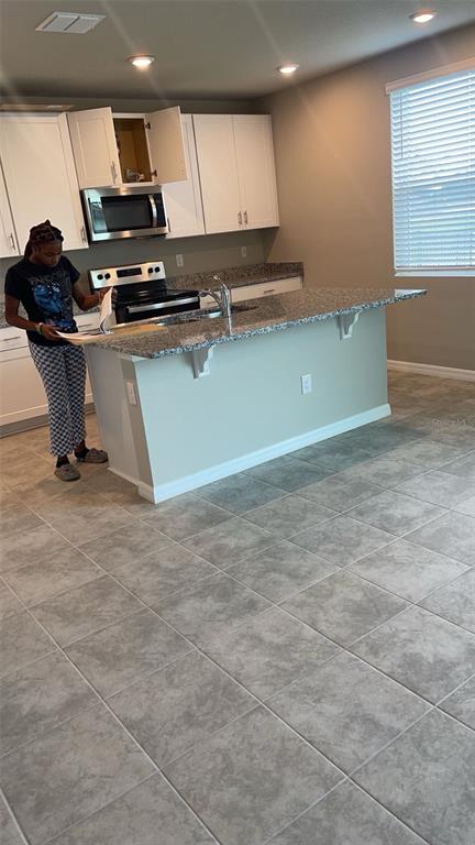 A kitchen features white cabinets, granite countertops, a center island, and gray tile flooring — 10217 DAYBREAK GLEN, PARRISH, FL