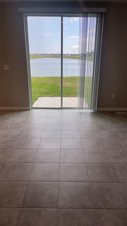 A room with light-colored tile flooring features a sliding glass door overlooking a pond — 10217 DAYBREAK GLEN, PARRISH, FL