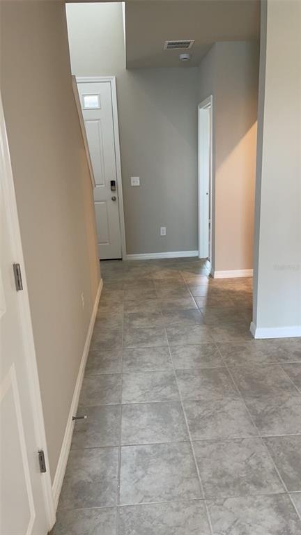 An entryway with gray tile flooring leads to a white front door and hallway — 10217 DAYBREAK GLEN, PARRISH, FL