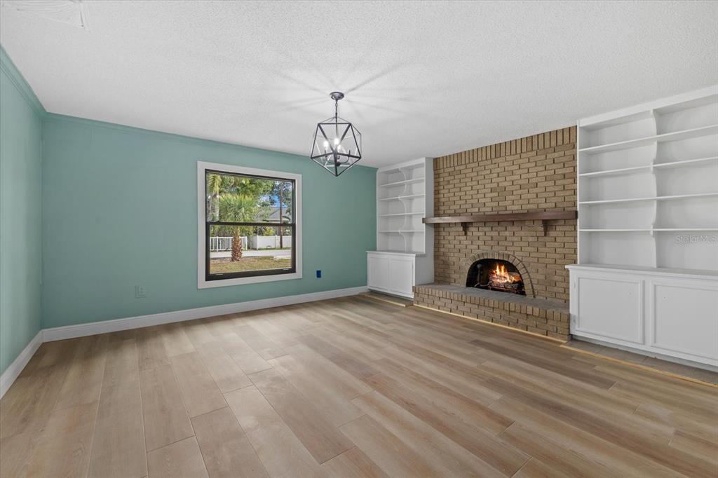 A living room features light wood floors, a teal wall, and a brick fireplace with shelving — 2818 OLYMPIC STREET, SARASOTA, FL