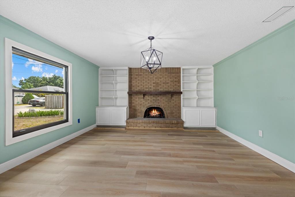 A living room features light green walls, wood-look flooring, a brick fireplace, and built-in shelves — 2818 OLYMPIC STREET, SARASOTA, FL
