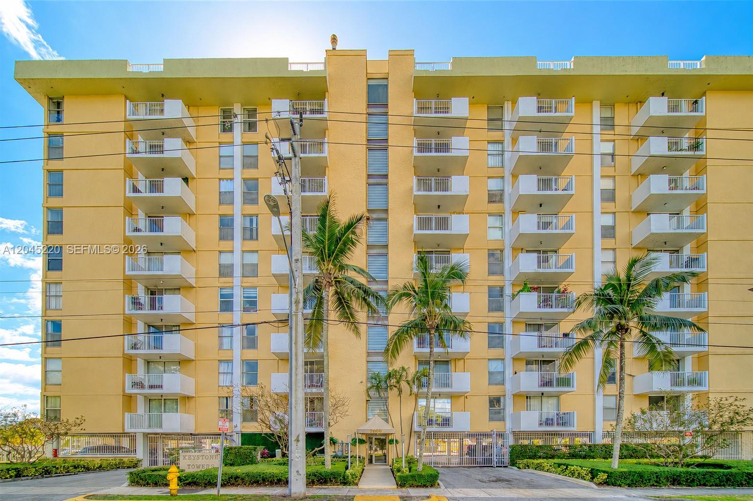 A multi-story yellow apartment building features white balconies and palm trees in the front — NORTH MIAMI, FL
