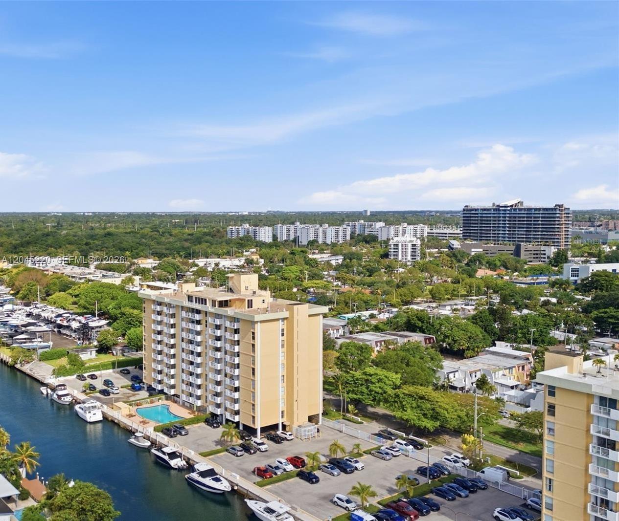 An aerial view shows a tall apartment building, a swimming pool, and a boat-lined canal — NORTH MIAMI, FL