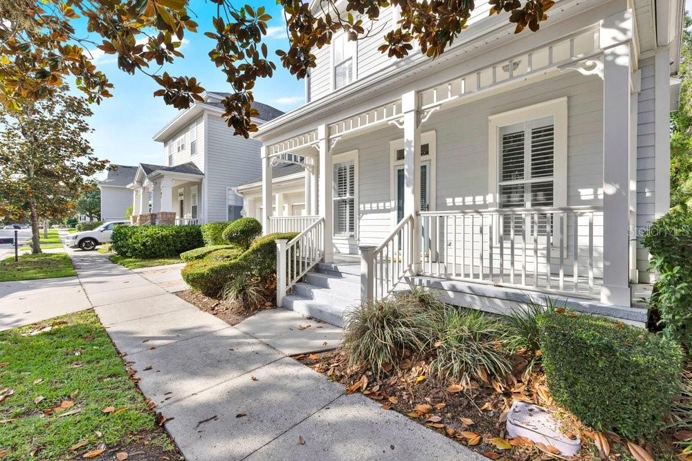 A light gray house with a front porch and white railings sits along a sidewalk — 1013 MAIDEN TERRACE, CELEBRATION, FL