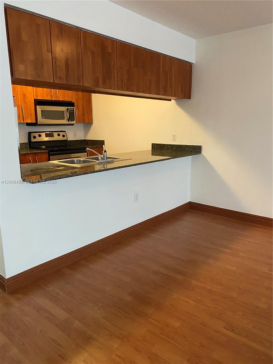 A kitchen with wood cabinets, granite countertops, and a breakfast bar overlooks a dining area — 1200 Brickell Bay Dr # 1914, Miami FL 33131, MIAMI, FL