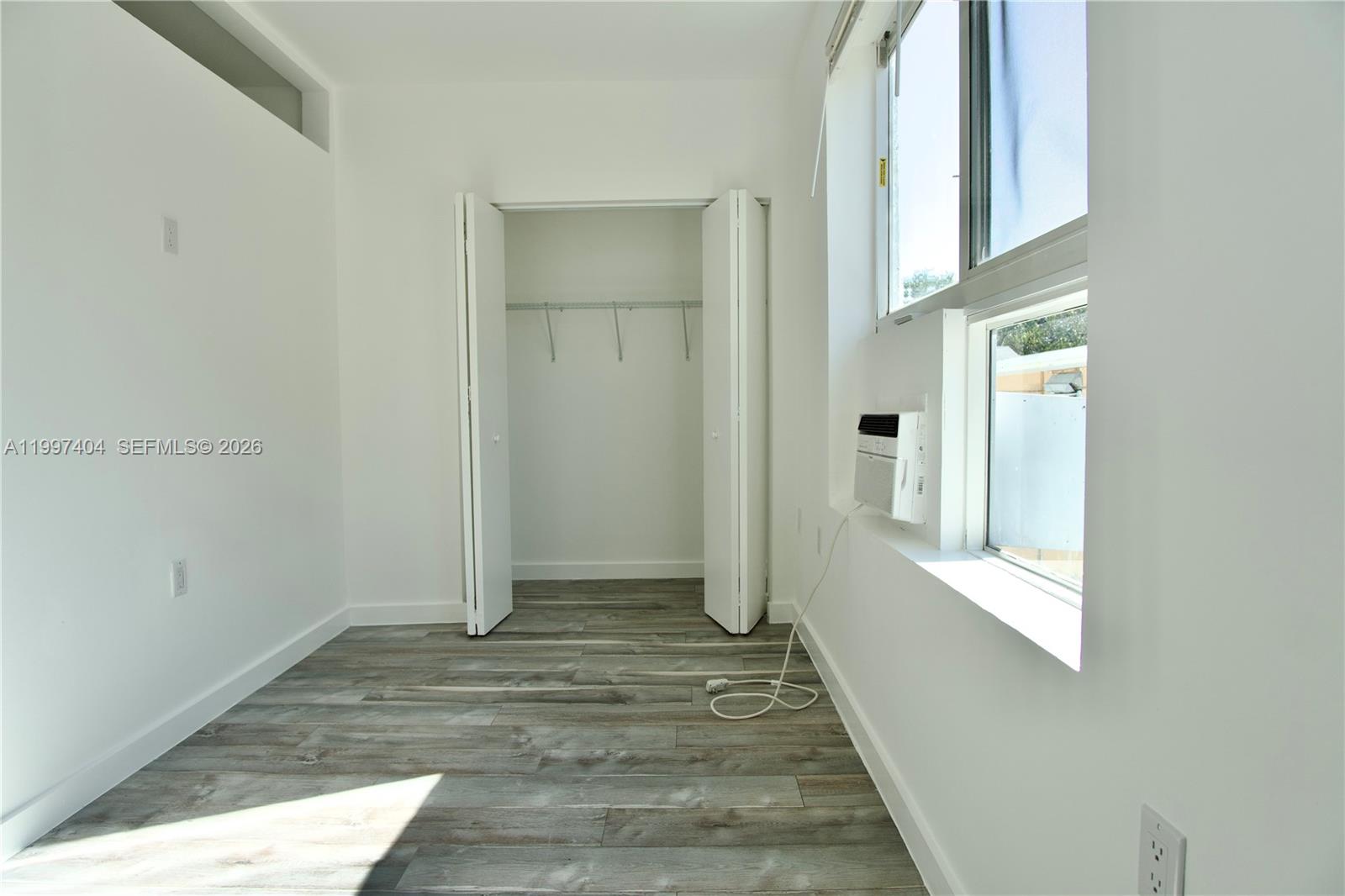 A small, white-walled bedroom features wood-look flooring, a closet, and a window air conditioner — 1036 SW 5th St # 12, Miami FL 33130, MIAMI, FL