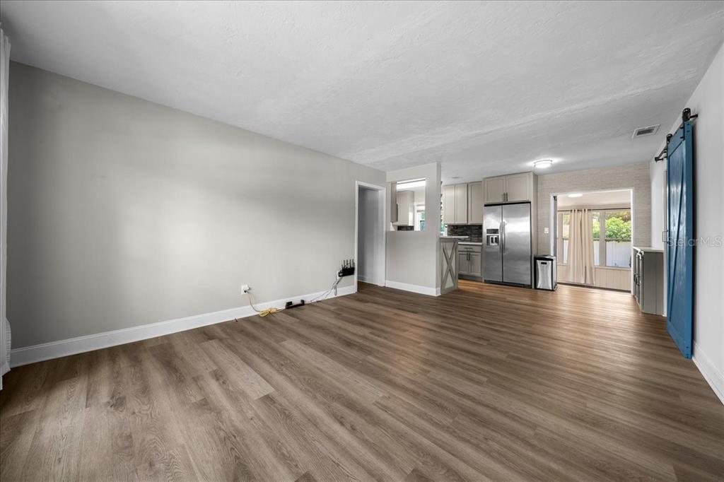 An open-concept living area with light wood-look flooring, gray walls, and a blue barn door — 2830 SE 6TH STREET, OCALA, FL