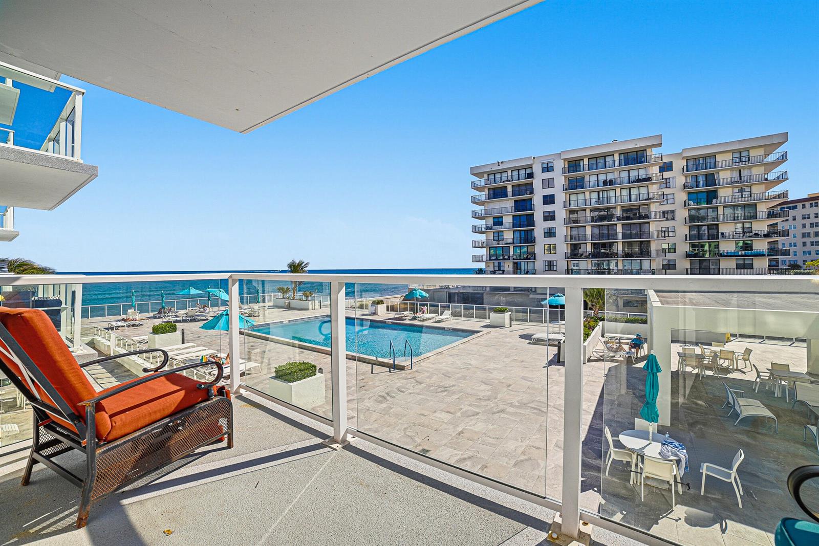 A balcony with an orange chair overlooks a swimming pool, patio, and the ocean — 3450 S Ocean Boulevard # 211, Palm Beach FL 33480, PALM BEACH, FL
