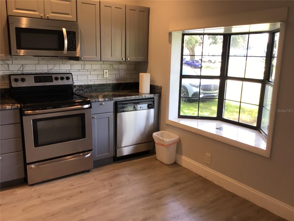 A kitchen features gray cabinets, stainless steel appliances, a tile backsplash, and a bay window — 1010 DAKOTA AVENUE, ST CLOUD, FL