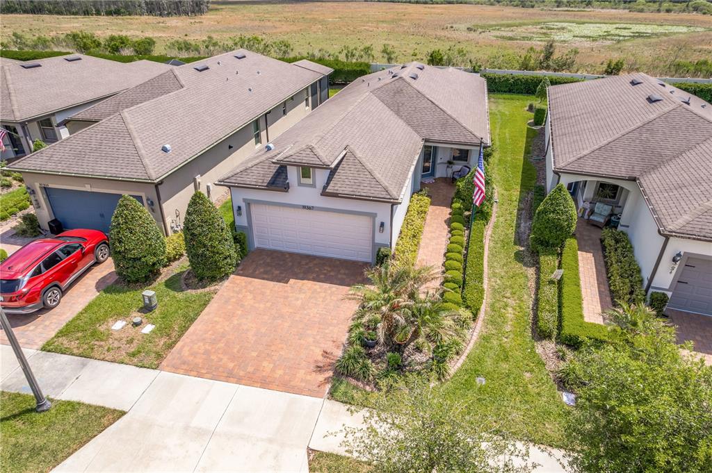 An aerial view shows three suburban houses with paved driveways and manicured landscaping — 19367 COASTAL SHORE TERRACE, LAND O LAKES, FL