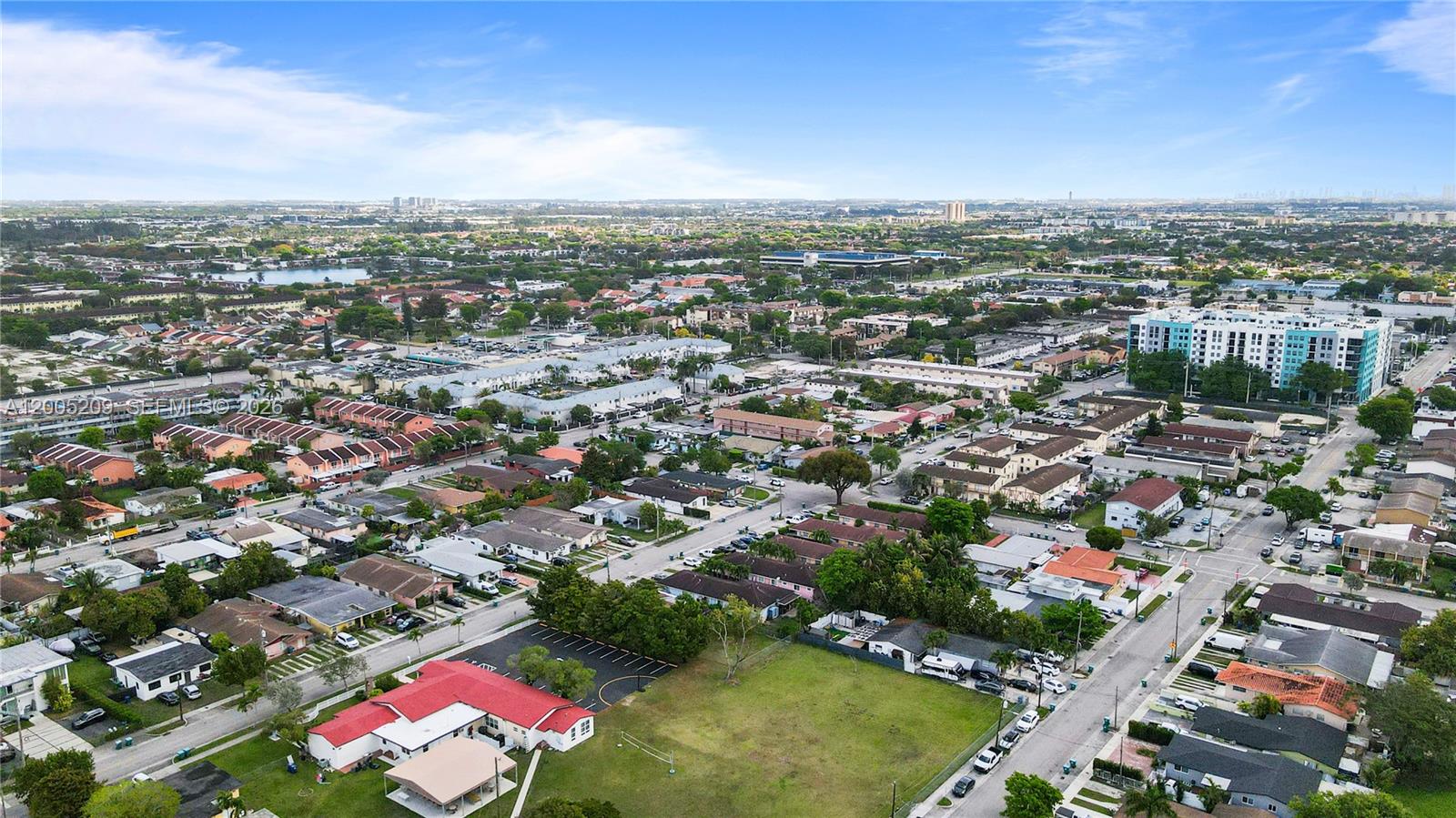 An aerial view shows a suburban neighborhood with houses, apartment buildings, and a grassy lot — 11002 SW 3rd St, Sweetwater FL 33174, SWEETWATER, FL