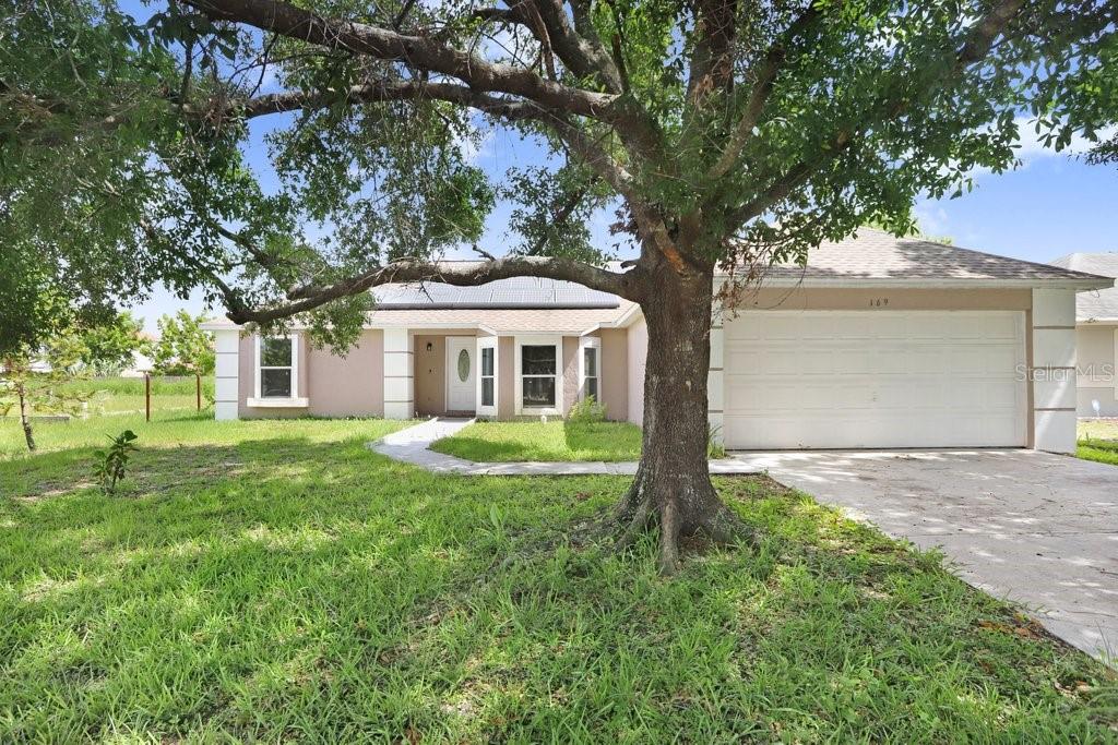 A single-story house with a two-car garage and a large tree in the front yard — 169 BIRMINGHAM DRIVE, KISSIMMEE, FL