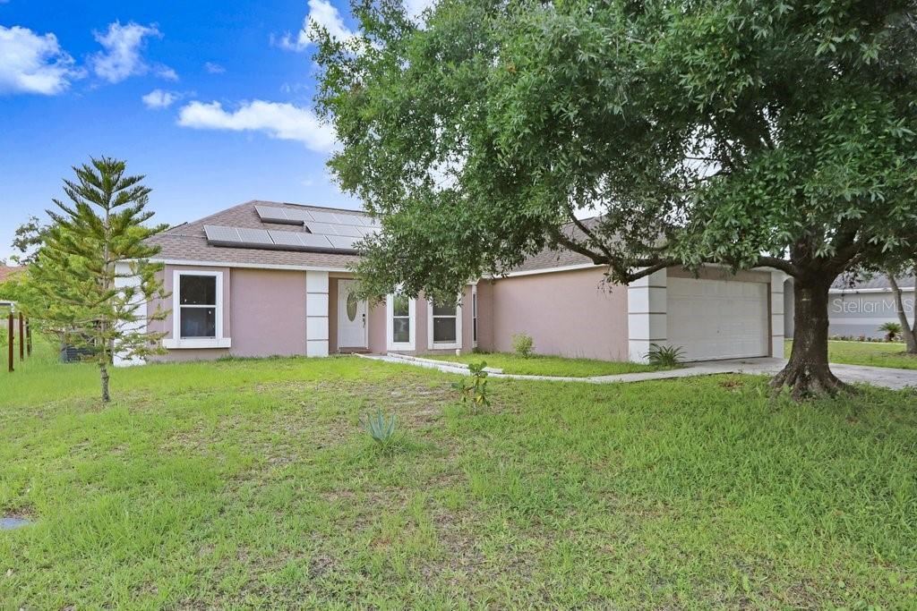 A single-story house with a tan exterior, a two-car garage, and solar panels on the roof — 169 BIRMINGHAM DRIVE, KISSIMMEE, FL