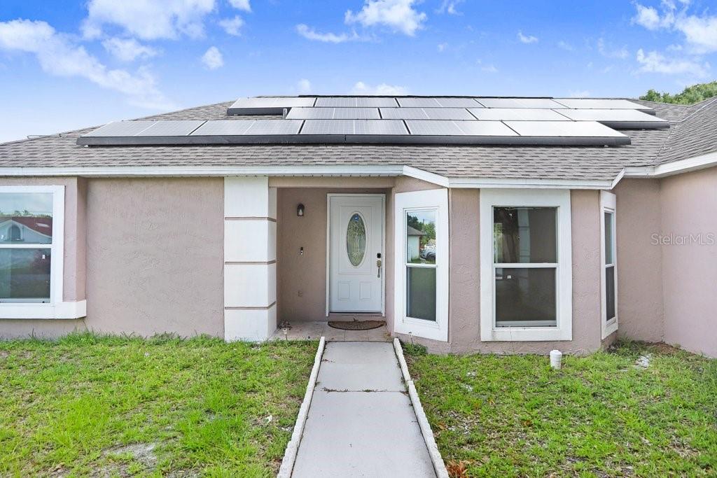 A single-story house exterior features a front walkway, a recessed entryway, and roof-mounted solar panels — 169 BIRMINGHAM DRIVE, KISSIMMEE, FL