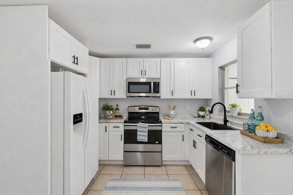 A kitchen features white cabinets, stainless steel appliances, a black sink, and marble-patterned countertops — 3640 MURROW STREET, NEW PORT RICHEY, FL