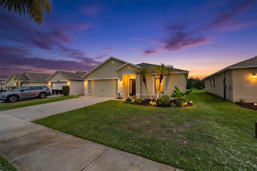 A single-story suburban house with a two-car garage and palm trees at sunset — 1319 TARTON WAY, COCOA, FL