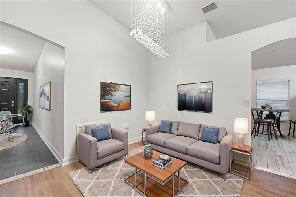A living room features a gray sofa, matching armchair, wood coffee table, and a crystal chandelier — 1319 TARTON WAY, COCOA, FL