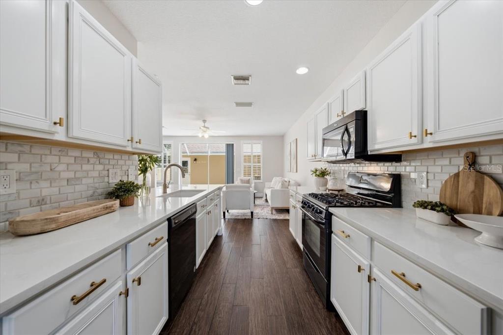 A galley kitchen features white cabinets, quartz countertops, a subway tile backsplash, and dark appliances — 9530 W PARK VILLAGE DRIVE, TAMPA, FL