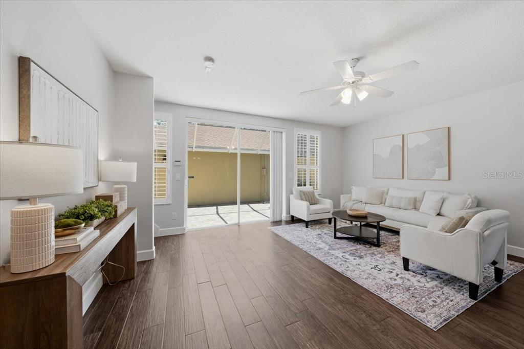A living room features wood-look flooring, a white sofa set, and sliding glass patio doors — 9530 W PARK VILLAGE DRIVE, TAMPA, FL