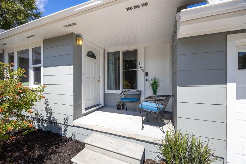 The exterior of a house features a gray-sided facade, a covered porch, and two chairs — 1024 MICHIGAN DR E, DUNEDIN, FL