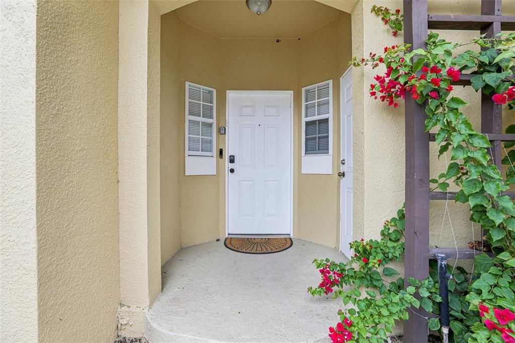 A beige exterior entryway features a white front door, two windows, and a wooden trellis — 8419 CRYSTAL COVE LOOP, KISSIMMEE, FL