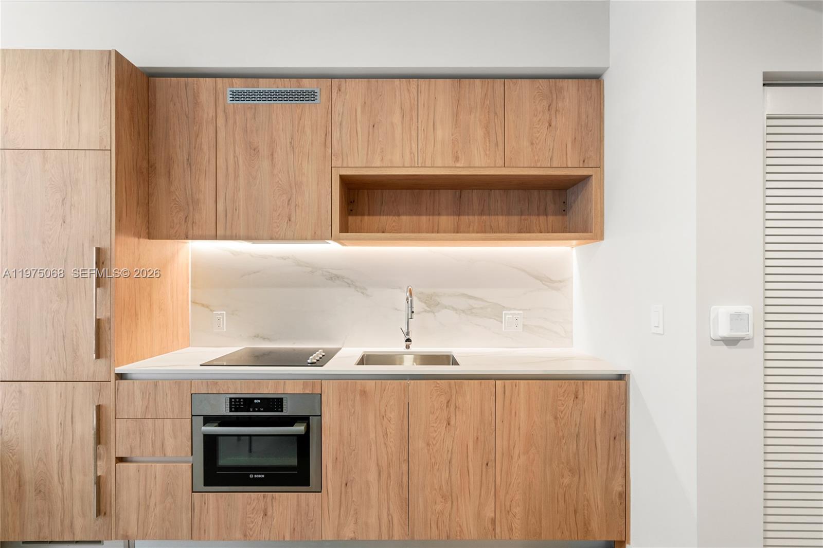 A modern kitchen features wood-grain cabinetry, a marble backsplash, and integrated stainless steel appliances — 11 NE 6th St # 2104, Miami FL 33132, MIAMI, FL