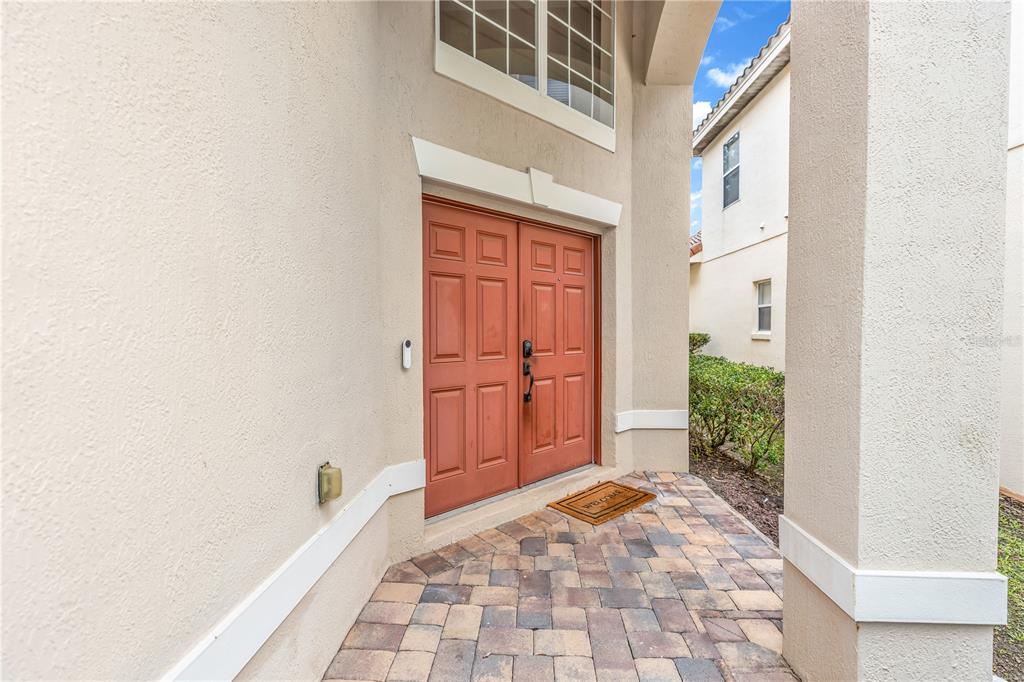 A front entrance with double red doors, a stone paver porch, and a stucco exterior — 6971 LUCCA STREET, ORLANDO, FL