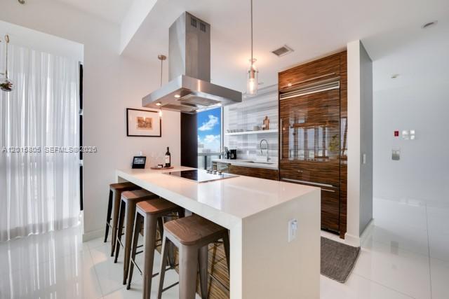 A modern kitchen features a white quartz island, bar stools, and wood-paneled cabinetry — 1100 Biscayne Blvd # 3205, Miami FL 33132, MIAMI, FL