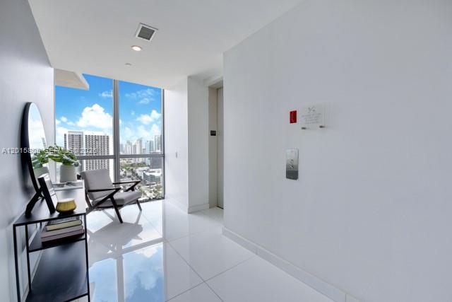 A bright hallway with white tile floors, a modern chair, and a view of city buildings — 1100 Biscayne Blvd # 3205, Miami FL 33132, MIAMI, FL