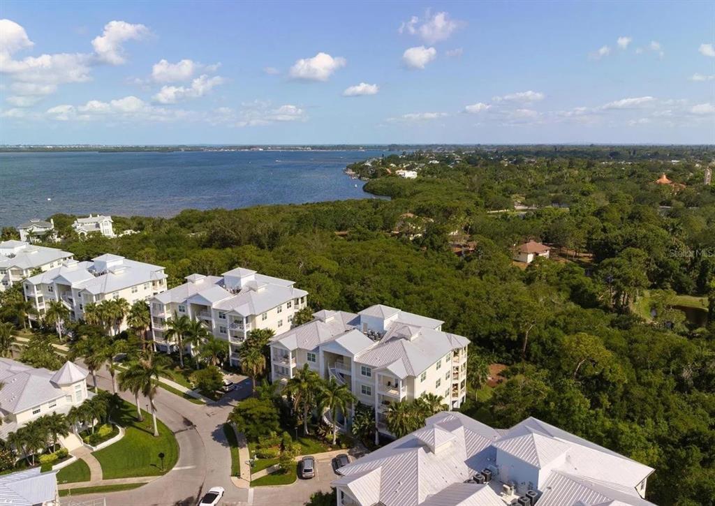 An aerial view shows multi-story residential buildings surrounded by dense trees near a large bay — 7710 34TH AVENUE W UNIT 101, BRADENTON, FL