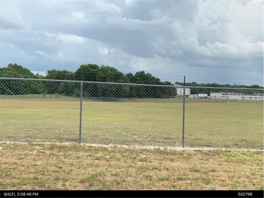 A chain-link fence encloses a large, flat, grassy field under a cloudy sky — TBD NW 126TH TERRACE, ALACHUA, FL