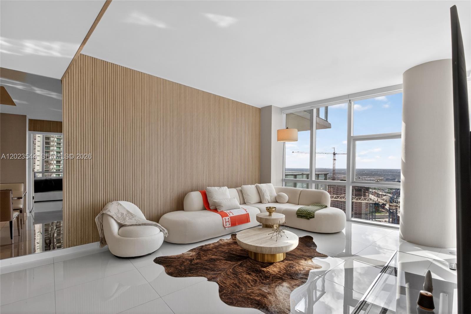 A modern living room features a curved white sofa, wood-slatted wall, and floor-to-ceiling windows — 851 NE 1st Ave # 3201, Miami FL 33132, MIAMI, FL