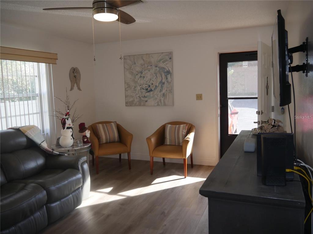 A living room features a grey leather sofa, two mustard chairs, and light wood flooring — 6165 CHESHAM DRIVE UNIT 5, NEW PORT RICHEY, FL