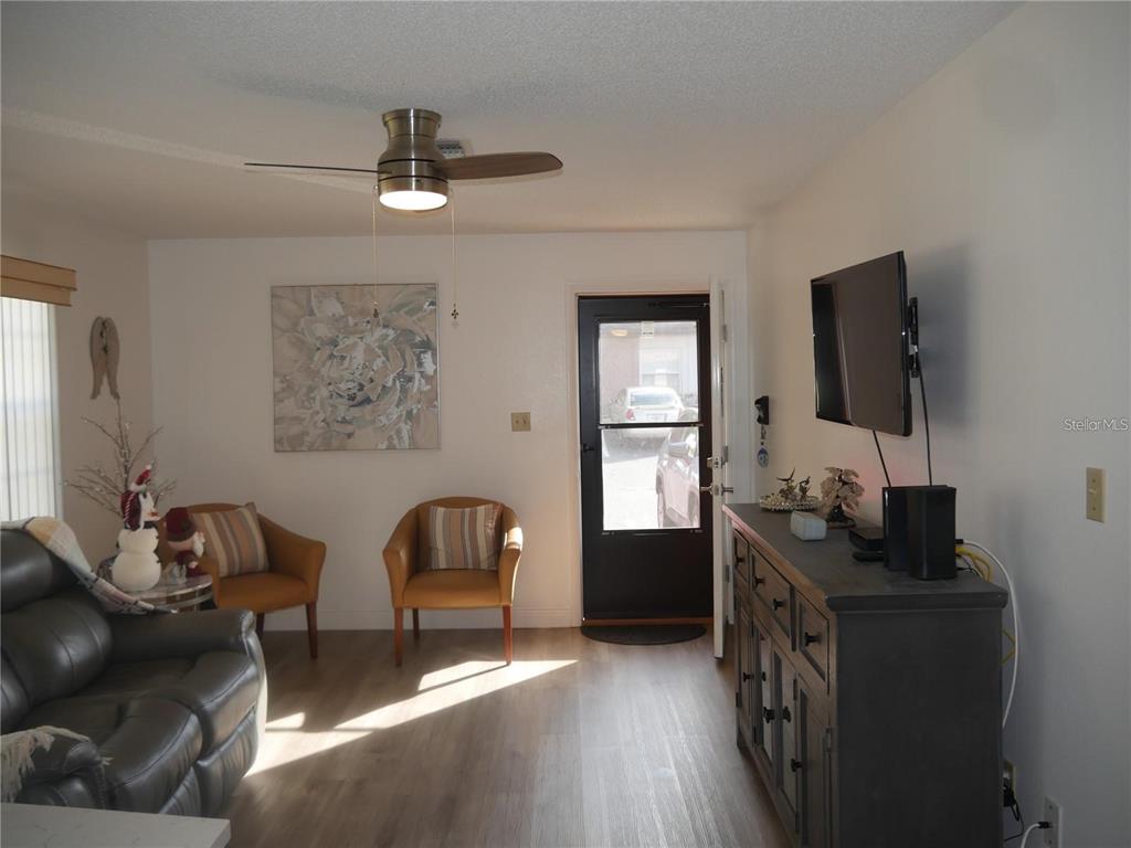 A living room features a gray sofa, two tan armchairs, a television, and wood flooring — 6165 CHESHAM DRIVE UNIT 5, NEW PORT RICHEY, FL