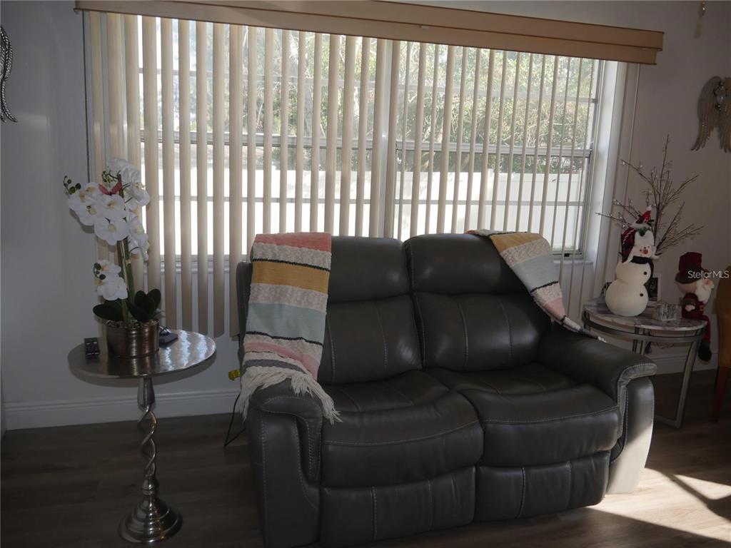 A gray loveseat sits in front of a window with vertical blinds in a room — 6165 CHESHAM DRIVE UNIT 5, NEW PORT RICHEY, FL