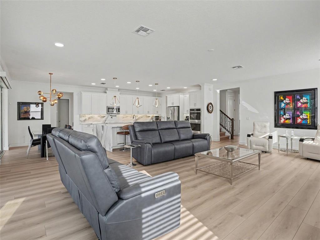 An open-concept living room and kitchen featuring gray leather sofas, light wood floors, and cabinetry — 2612 RAVENCLIFFE TERRACE, OVIEDO, FL