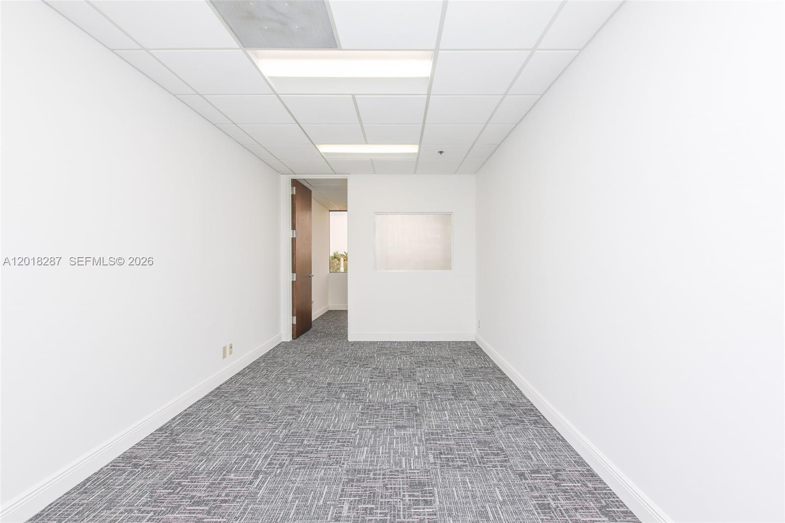 An empty office features white walls, gray patterned carpet, drop ceiling lights, and a doorway — 1900 Glades Rd # 357, Boca Raton FL 33431, BOCA RATON, FL