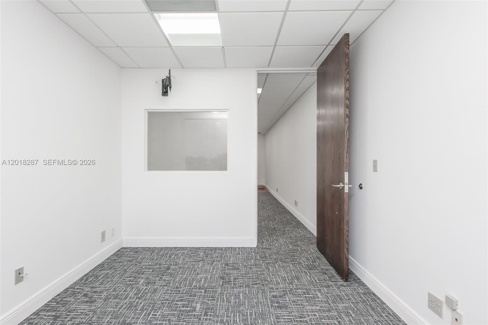 An office room features white walls, a gray patterned carpet, and a wooden door — 1900 Glades Rd # 357, Boca Raton FL 33431, BOCA RATON, FL