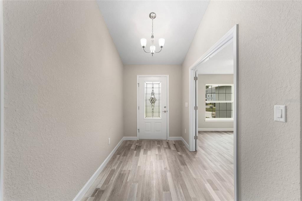 A bright entryway features light wood-look flooring, a white front door, and a hanging chandelier — 4190 SW 98TH STREET, OCALA, FL