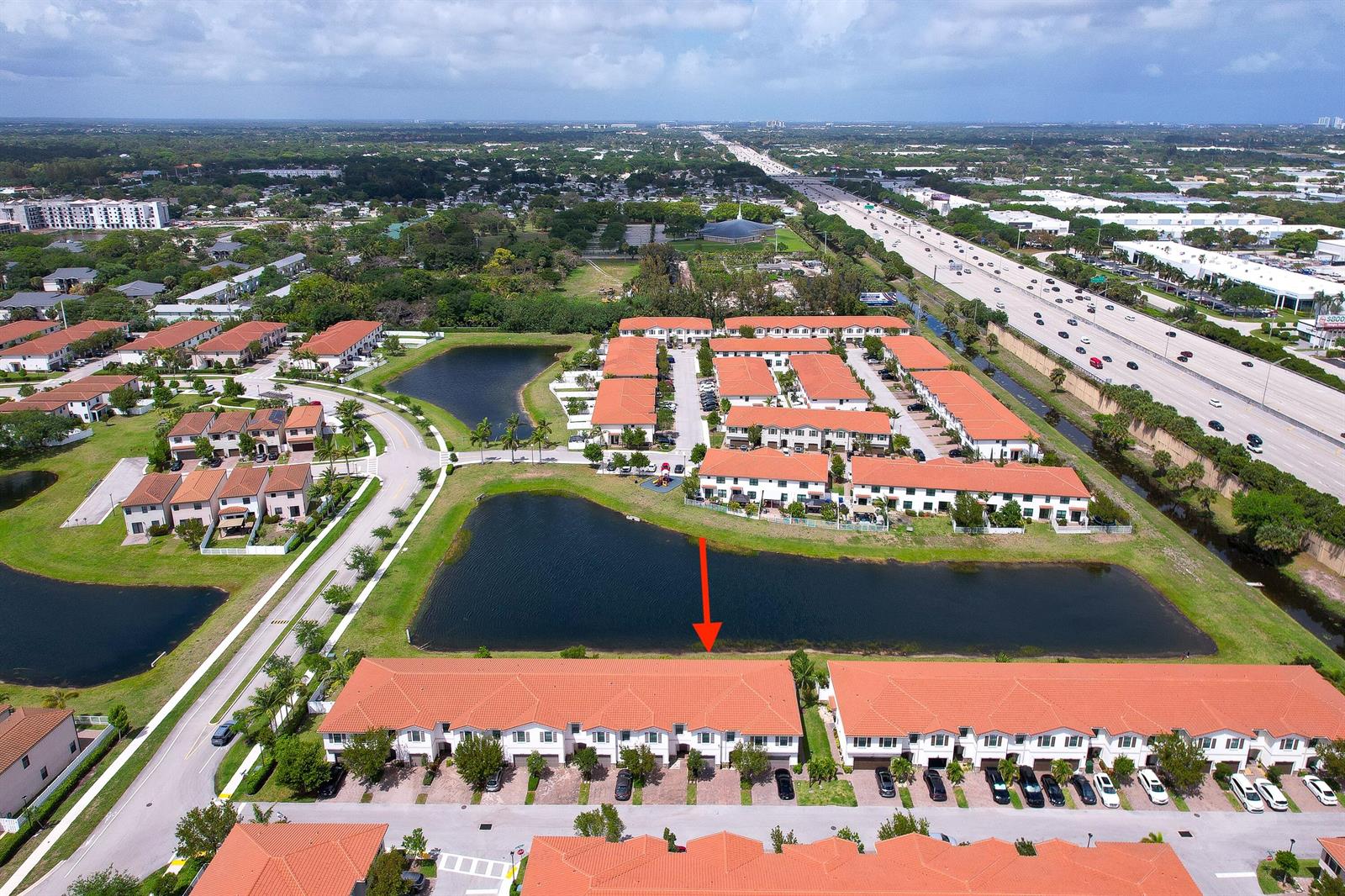 An aerial view shows a residential townhouse complex with red-tiled roofs and a central lake — 2024 Sugar Maple Drive, Riviera Beach FL 33410, RIVIERA BEACH, FL