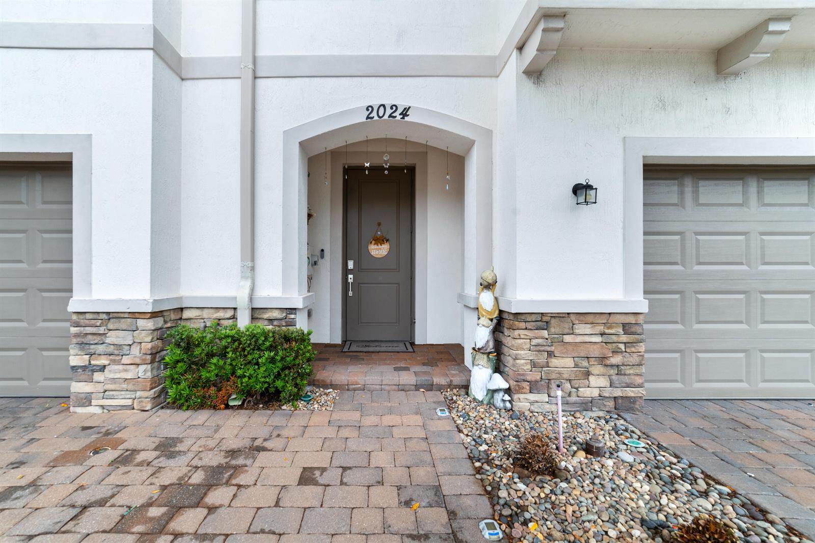 The exterior of a home features a brown front door, stone accents, and a paver walkway — 2024 Sugar Maple Drive, Riviera Beach FL 33410, RIVIERA BEACH, FL