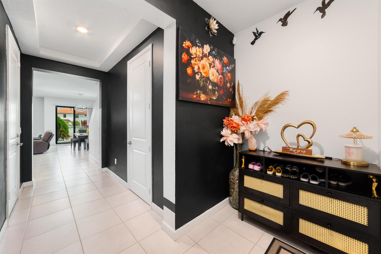 An entryway features a black accent wall with floral art, a shoe cabinet, and tile flooring — 2024 Sugar Maple Drive, Riviera Beach FL 33410, RIVIERA BEACH, FL
