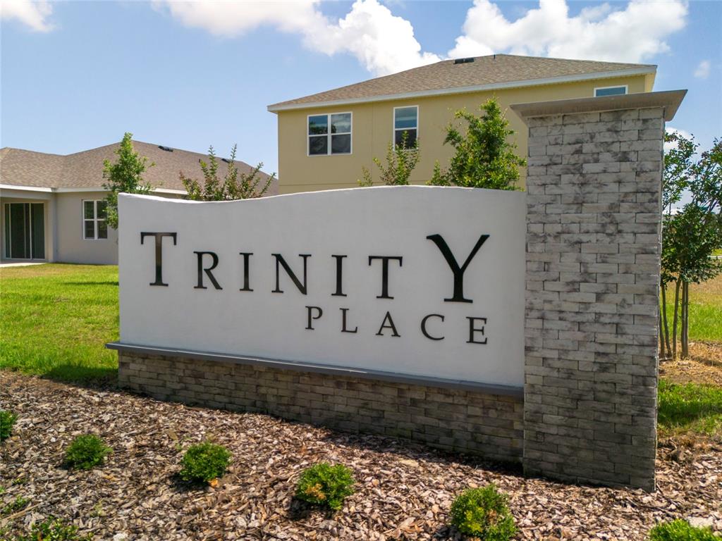 A stone and stucco monument sign for Trinity Place stands in front of residential houses — 6079 VISION ROAD, ST CLOUD, FL