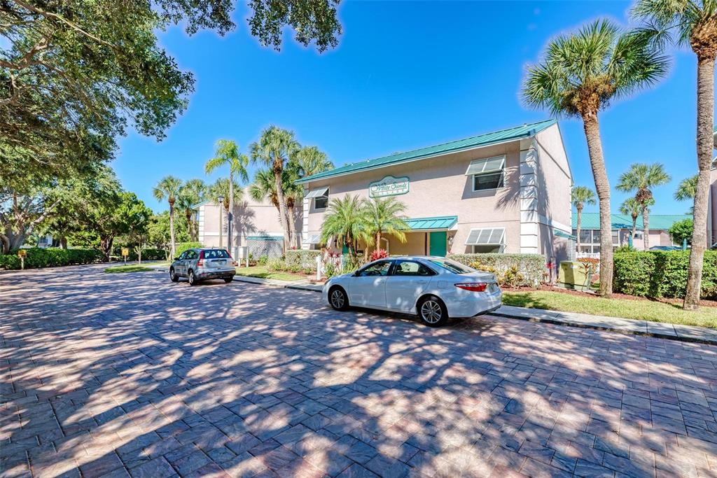 A white sedan is parked in front of a two-story apartment building with palm trees — 5683 MIDNIGHT PASS ROAD UNIT 105, SARASOTA, FL