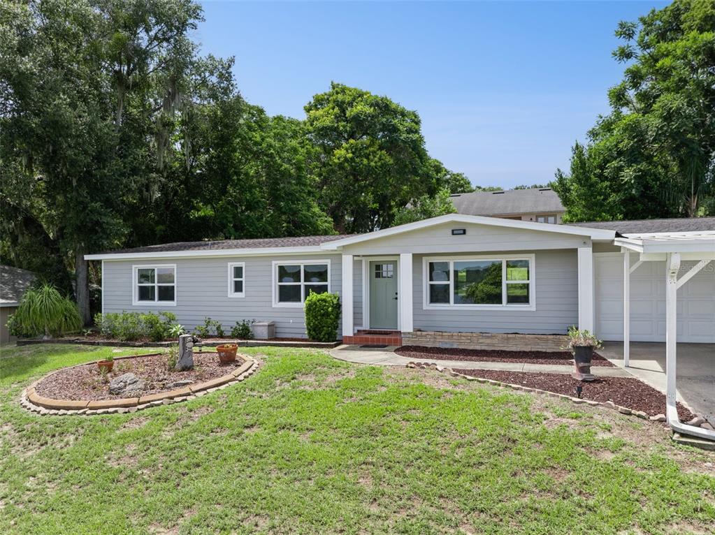 A single-story house with light gray siding, a green front door, and a carport — 1024 SUNSET DRIVE, LAKE WALES, FL