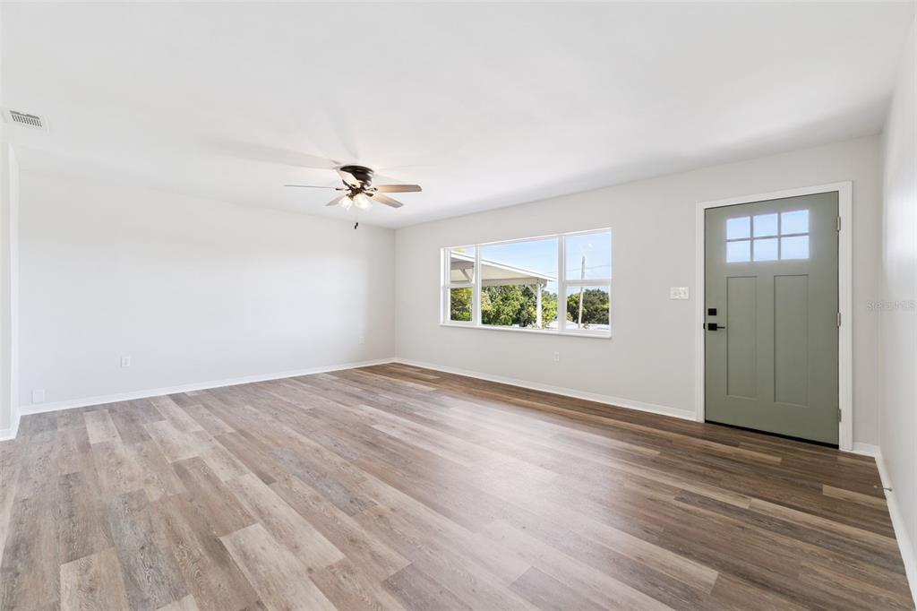 A living room with light gray walls, wood-look flooring, a ceiling fan, and a green door — 1024 SUNSET DRIVE, LAKE WALES, FL